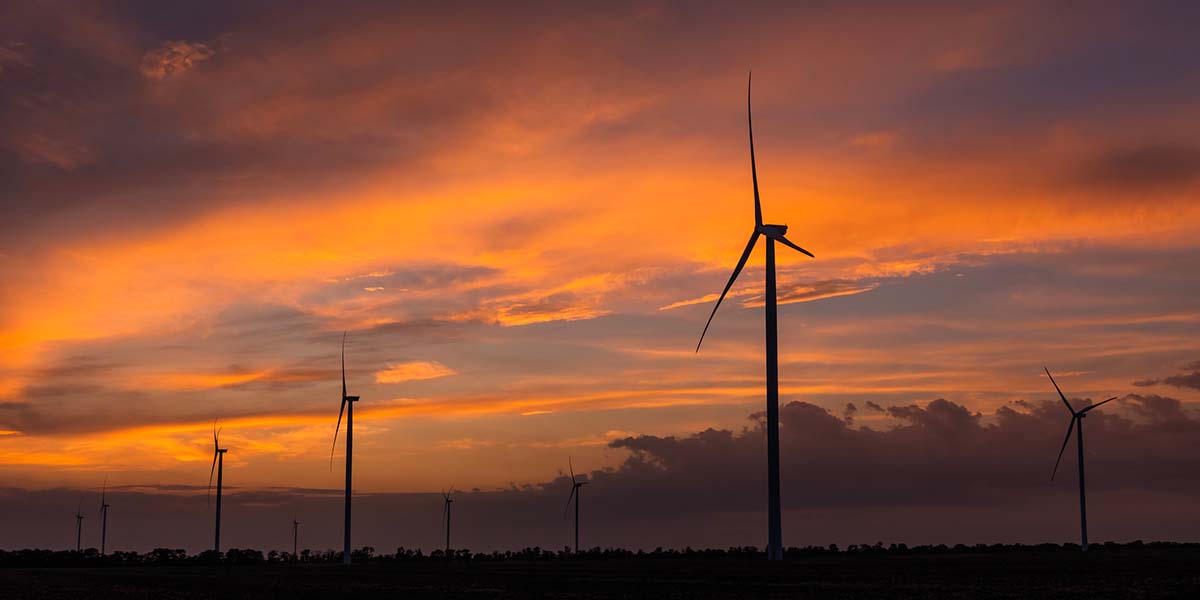 Wind turbines in a field at sunset with cloudy skies overhead.